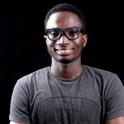 A Black man wearing a grey t-shirt and glasses, smiling towards the camera